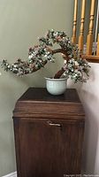 Full frontal view of the handmade glass floral arrangement displayed on a wooden cabinet against a neutral wall and staircase railing.