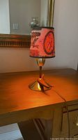 Small MCM style table lamp on wood surface with lit decorative shade showing vintage style print.