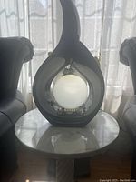 Full view of the black tear drop shaped lamp with a central frosted globe light, sitting on a white marble round table.