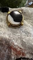 Close-up photo of the front of the round agate pin showing the banded black and white stone and gold-tone prong setting.