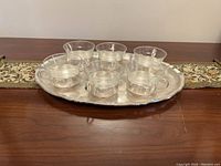 Set of 6 glass cups with silver plated holders on a matching silver plated tray on patterned table runner.