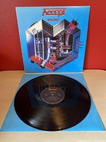 Full view of vinyl record with album cover behind it showing mechanical heart artwork on blue background.