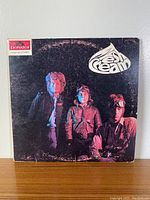 Front cover of the cream vinyl album 'Fresh Cream' 1966 showing the three band members and the band logo on a black background.