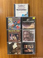 Front view of the seven CD cases arranged in two rows on a wooden surface.