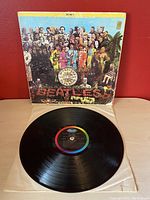 Front cover of Sgt. Pepper's Lonely Hearts Club Band vinyl LP showing the classic colorful collage of figures and the band's name spelled out in flowers.