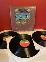 Photo showing the front gatefold album cover with Yes artwork and three vinyl records laid out in front.