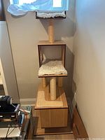 Front view of the wooden cat tree showing the plush fabric cushions on each level, sisal-wrapped scratching posts, and cubed enclosure with circular cutout.