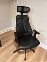 Front view of black office/gaming chair with mesh back and headrest, padded seat with red lining, armrests, on five caster wheels.