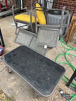 Outdoor patio furniture set with coffee table, two yellow cushioned chairs, mini sofa, and black fan stacked outdoors on concrete surface