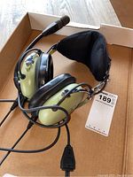 Full view of olive green headset with boom mic and cord in cardboard box