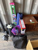 Photo showing all camping related items together including kite box, air mattresses, plastic dishware in net bag, and wooden tote.