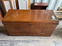 Front view of the cedar chest showing the rectangular shape, wood veneer top with some wear, and the front panel design.