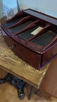 Wooden charging station showing four padded slots separated by wooden dividers with small drawer below on wooden table.