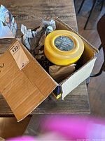 Yellow 1/2 ton chain hoist in original open box on brown table with paper packing inside.