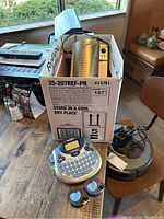 Box containing a silver laminating machine and Dymo LetraTag label maker with two cartridges on table.