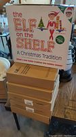 Five stacked boxes of flexible LED rope lights with visible labelling and packaging, and one boxed Elf on the Shelf set on top