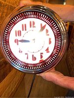 Front view of the 14 inch round neon wall clock lit up in red neon light, showing the clock face with stylized numbers and hands.