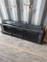 Two folded black metal Erickson ramps with mesh surface and handles, leaning against a shipping container wall.