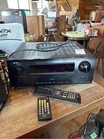 Front view of Denon AVR-2808CI AV Surround Receiver on wooden surface with two remote controls placed in front, one smaller and one longer.