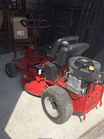 Three-quarter view of mower showing red deck, black seat, handlebar and engine at rear