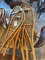 Three pairs of wooden snowshoes with webbing placed on a table, showing different sizes and the natural wood construction without bindings.