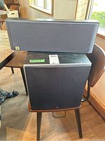 Polk Audio PSW10 subwoofer and JBL SC305 speaker displayed together on chairs showing size and shape.