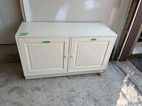 Front and side view of white laminate cabinet showing double paneled doors and wear on edges.