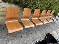 Photo showing six Ikea Gilbertdining stackable chairs lined up outdoors with metal legs and wooden seats and backs.