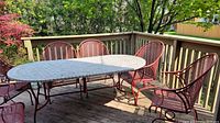 Wide view of six red metal mesh chairs arranged around a deck table on a wooden deck