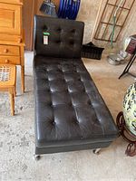 Full view of black leather tufted chaise lounge with metal legs on casters in garage setting.