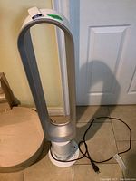 Full front view of the Dyson Cool bladeless tower fan upright on tiled floor with power cord