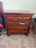 Front view of wooden end table showing three drawers with dark knobs and rounded feet.