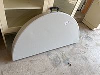 Semi-circle folded white folding table resting against a cabinet, showing the plastic textured surface and general shape.