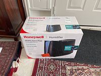 Boxed Honeywell humidifier showing brand and product type on side, placed on carpet near door.
