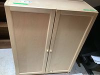 Front view of light wood IKEA cabinet with two doors, simple panel style, and round wooden knobs.