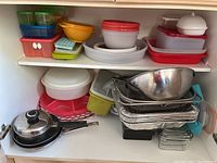Overview of lower cabinet contents showing stacked plastic storage containers, metal mixing bowls, foil pans, and kitchen trays.
