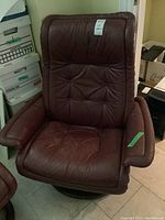 View of brown leather armchair showing padded armrests, tufted seat and back cushions, and wooden swivel base.