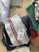 Stack of towels and throws beneath chairs showing a white tea towel with black dot and red/black stripe pattern on top
