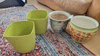 Four ceramic plant pots displayed on floor: two green square pots, one Asian floral with bird pattern, one Italian poppy floral pot