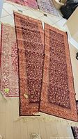 Two matching polyester runner rugs laid side by side on wooden floor showing burgundy floral pattern and beige fringe.