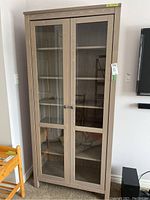 Front view of 6-tier wood bookshelf cabinet with glass double doors and metal knobs.