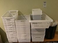 Stacked white plastic storage baskets against a wall