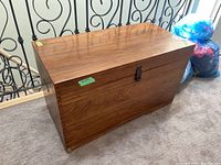 Wooden rectangular storage trunk with top closed, visible wood grain, and metal latch on front side.