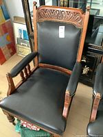 Front view of vintage carved mahogany chair with black leather upholstery and brass nailhead trim.