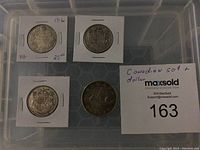 Four Canadian silver coins in cardboard holders within a plastic storage container: 1916 50 cent coin, two 1947 50 cent coins, and a 1936 silver dollar.