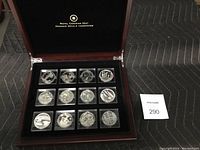 Cherry wood display box open showing 12 silver proof coins in plastic capsules arranged in three rows of four