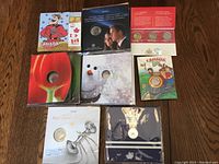 Top-down view of 8 Royal Canadian Mint coin sets on wooden table, colorful illustrative covers, all sealed in original packaging.
