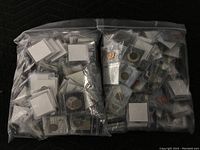 Two large resealable plastic bags filled with 2×2 cardboard flips each containing a coin and event image card, laid out on a black padded surface.