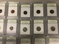 Top-down photo showing rows of graded US coins in hard plastic holders with INB certifications, coins ranging from pennies to quarters.