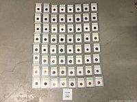 Lot of 64 USA graded coins arranged flat on the floor, individually encased in plastic holders with white label tops showing grading details by INB.